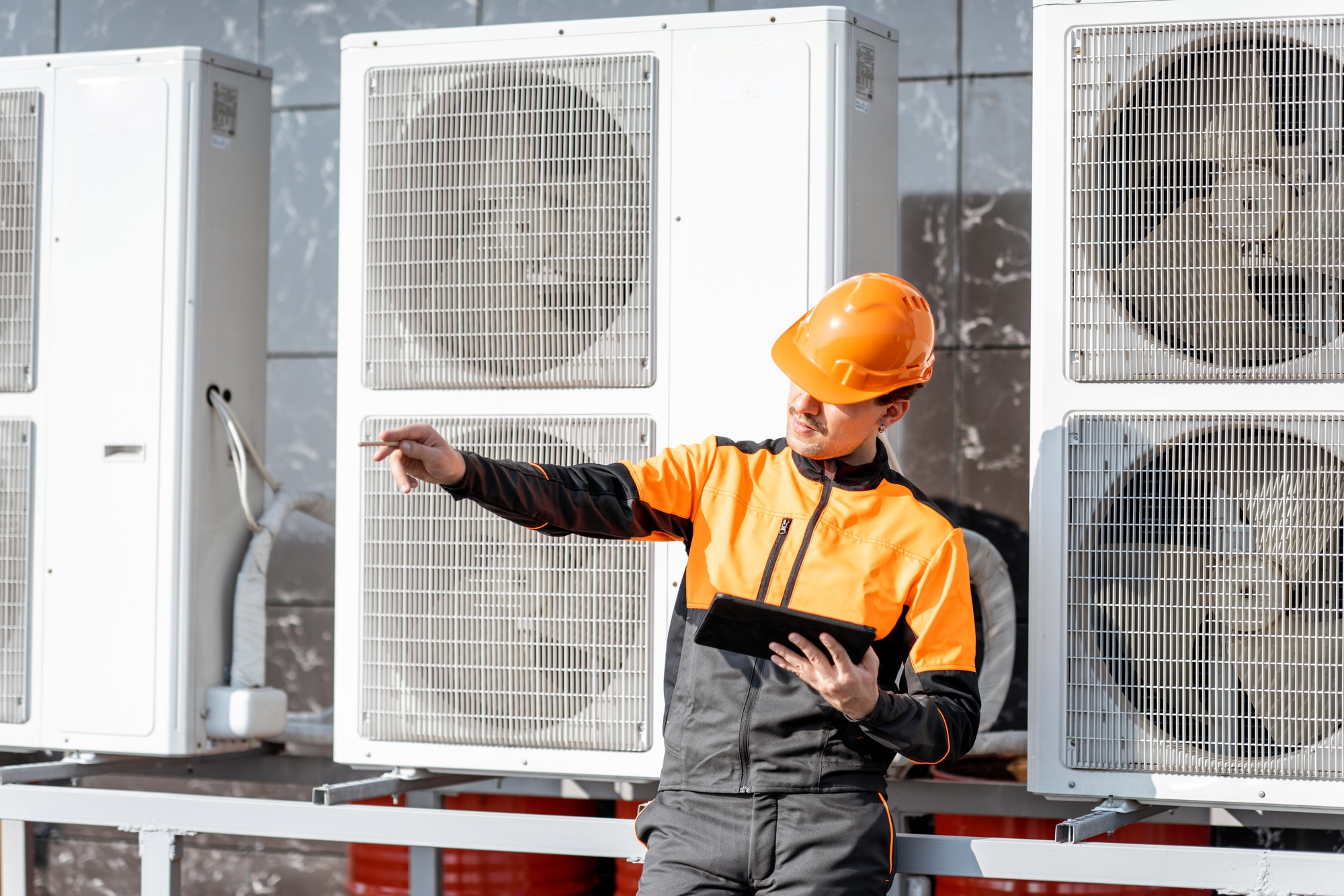 Workman servicing air conditioning or heat pump with digital tablet