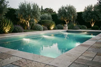 Piscine extérieure avec éclairage LED sous-marin turquoise au crépuscule entourée de dalles en pierre naturelle et de végétation méditerranéenne