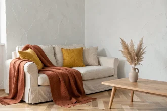 Salon minimaliste scandinave avec canapé en lin crème agrémenté d'un jeté en laine terracotta et de coussins jaune moutarde sur parquet en chêne clair